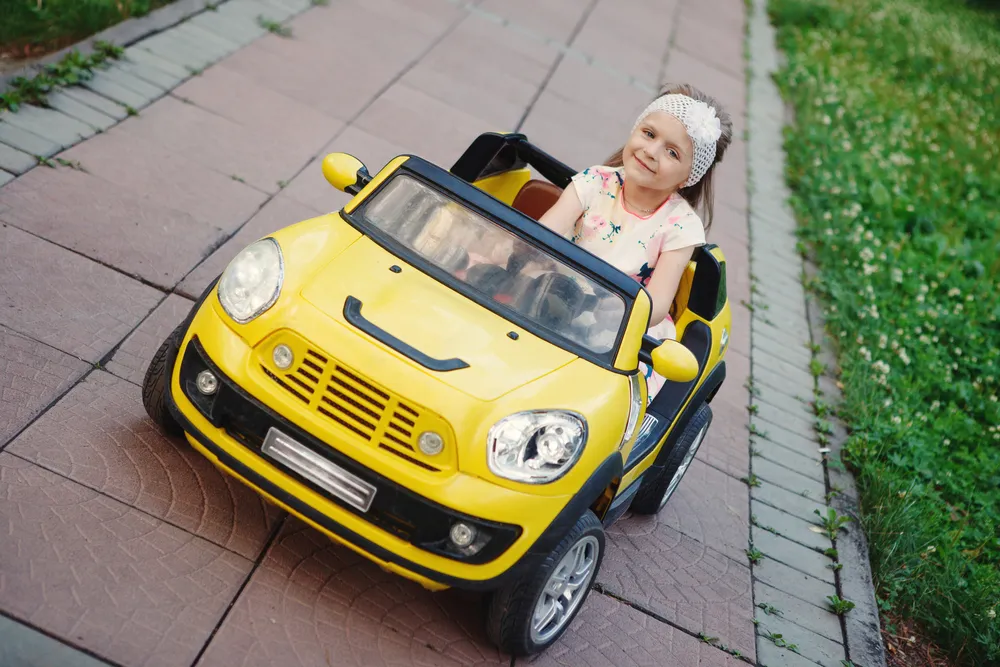 Little girl rides on toy electric car yellow in the Park